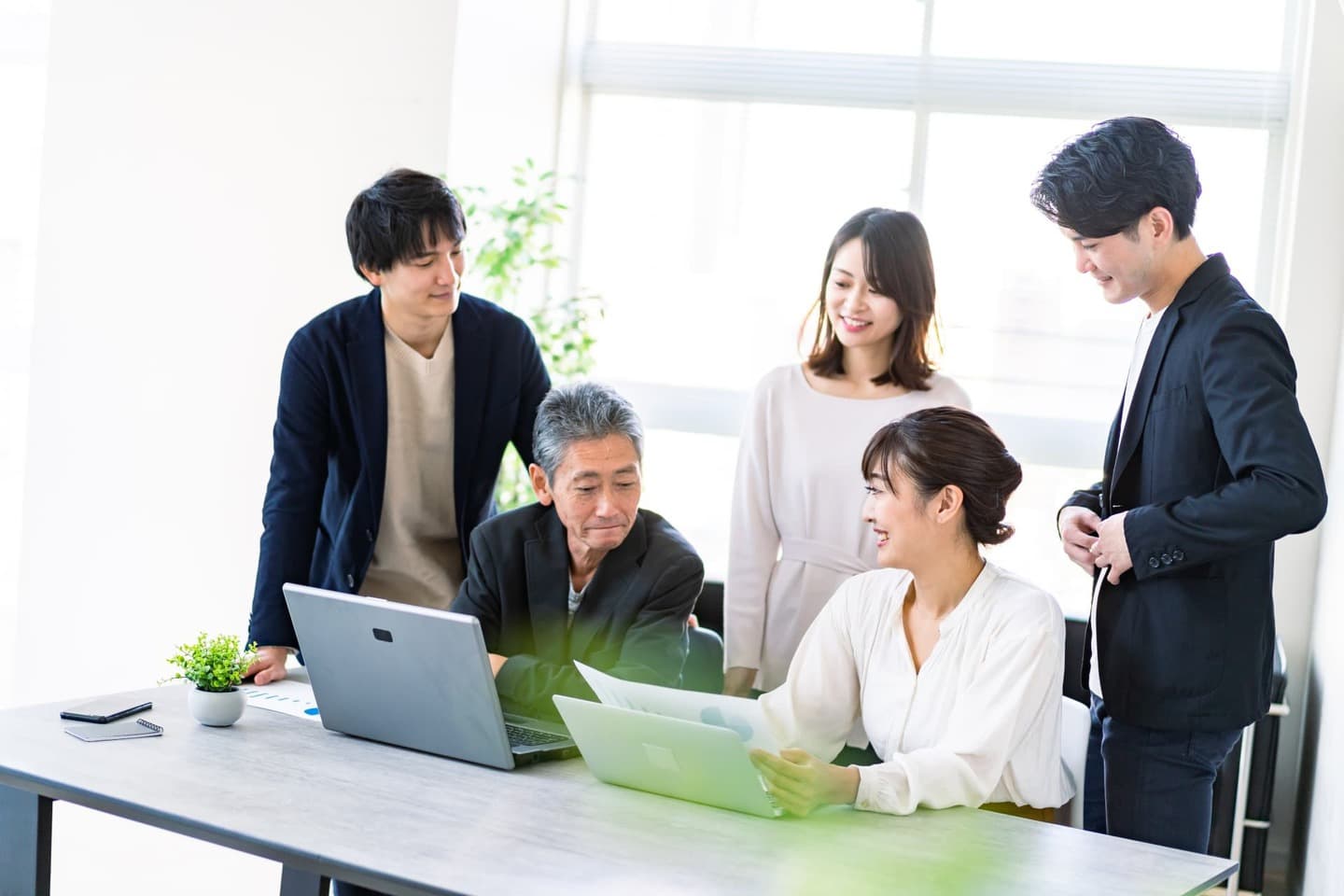 笑顔で集まってITツールの使い方を学ぶオフィスの従業員と経営者